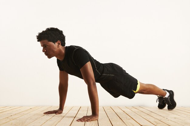 Serious fit black African American man effectuant une poussée de plancher en bois clair contre un mur blanc