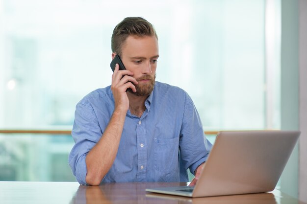 Serious Man Calling sur téléphone et de travail sur ordinateur portable