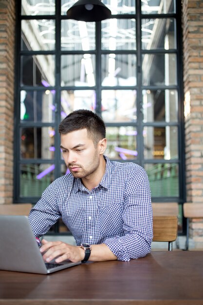 Serious Young Man Working on Laptop in Cafe