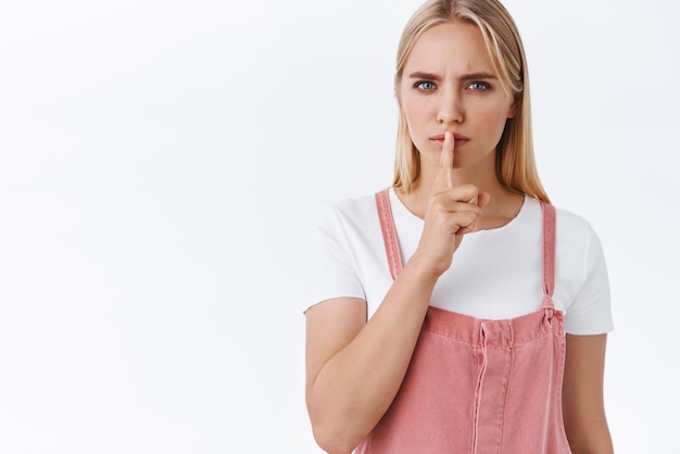 Seriouslooking jeune femme aux yeux bleus tatoués chut presse le doigt sur les lèvres et sillonne les sourcils demande le silence dit calme s'il te plait veux garder le secret pour que personne ne le dise sur fond blanc