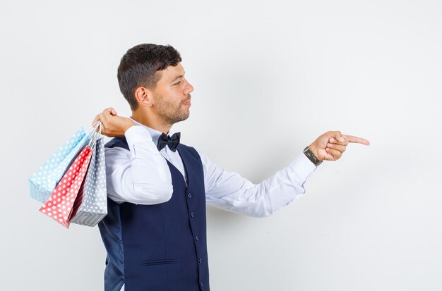 Serveur en chemise, gilet pointant vers l'avant avec des sacs en papier et l'air joyeux.