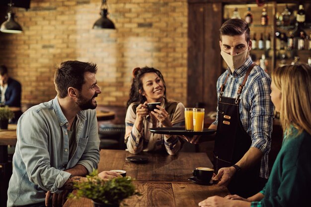 Serveur avec masque protecteur servant du café aux clients dans un pub