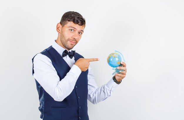 Serveur pointant sur le globe terrestre en chemise, gilet et à l'optimiste, vue de face.