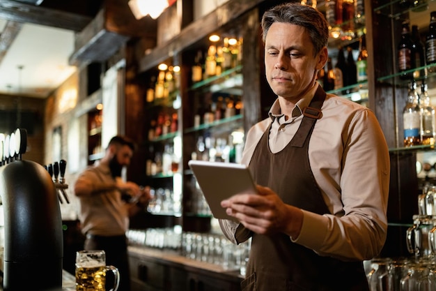 Serveur souriant à l'aide d'un pavé tactile tout en travaillant dans un bar