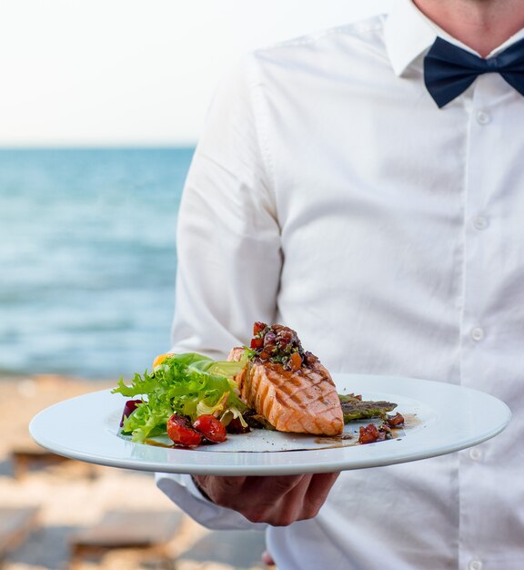 serveur tenant une assiette de saumon fumé grillé avec laitue, tomate, poivron