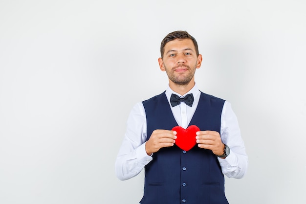 Serveur tenant un coeur rouge en chemise, gilet et à la gaieté. vue de face.