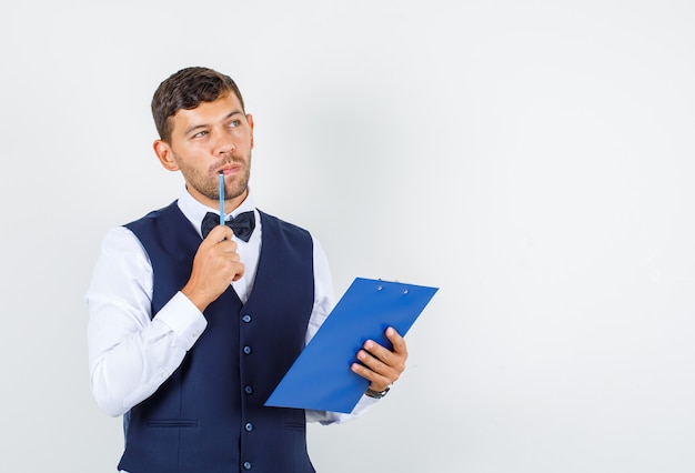 Serveur tenant le presse-papiers et un crayon en chemise, gilet et à la pensif, vue avant