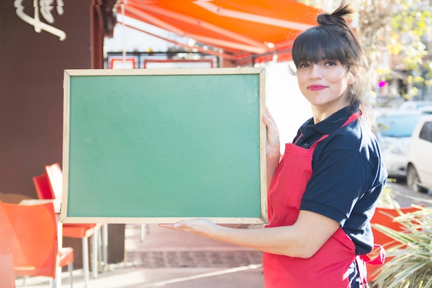 Photo gratuite serveuse femme confiant tenant tableau de menu vert blanc à l'extérieur