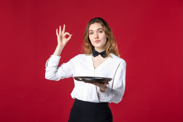 serveuse femme papillon sur le cou et tenant un plateau faisant un geste de lunettes sur fond rouge