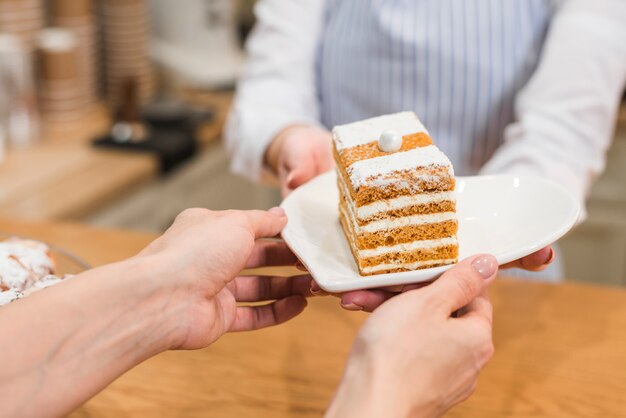 Une serveuse servant une pâtisserie sur une assiette blanche au client