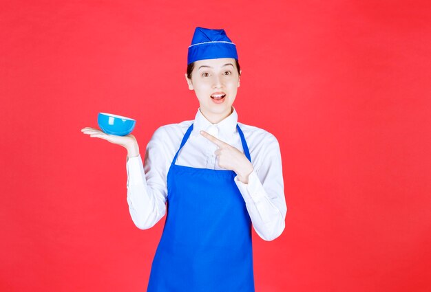 Serveuse en uniforme debout et pointant vers un bol sur le mur rouge.