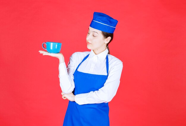 Serveuse en uniforme debout et tenant un bol sur le mur rouge.