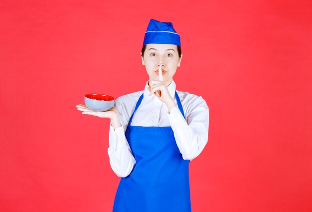 Serveuse en uniforme debout et tenant un bol sur le mur rouge.