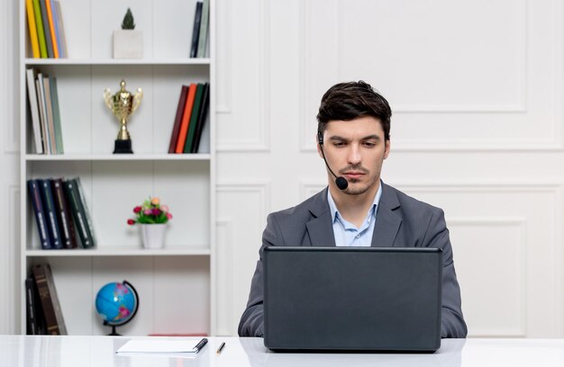 Service client bel homme en costume gris avec ordinateur et casque pensant sérieusement