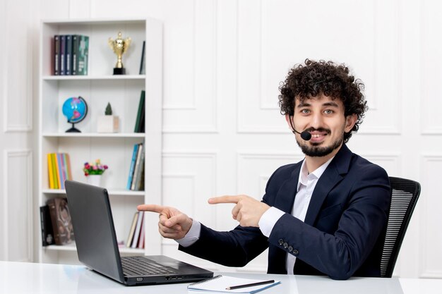 Service à la clientèle bel homme bouclé en costume de bureau avec ordinateur et casque souriant