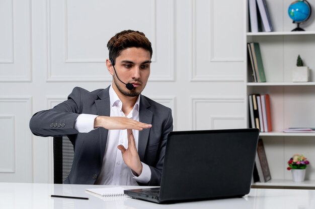 Service à la clientèle joli gentleman avec ordinateur en costume de bureau gris montrant le geste d'arrêt