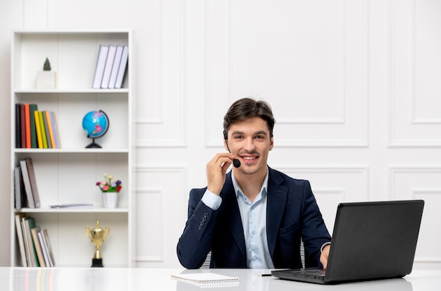 Service à la clientèle le joli mec brune en costume avec ordinateur portable avec le microphone et les écouteurs