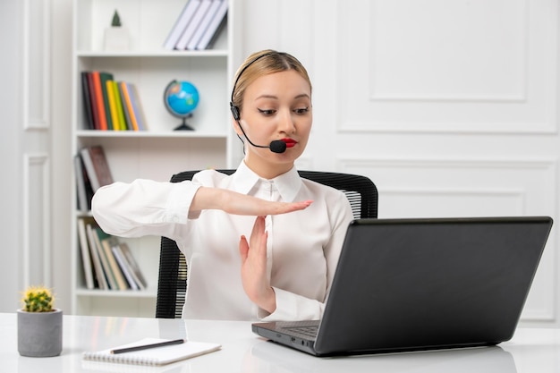 Service à la clientèle jolie belle fille en chemise blanche avec ordinateur et casque montrant le signe d'arrivée