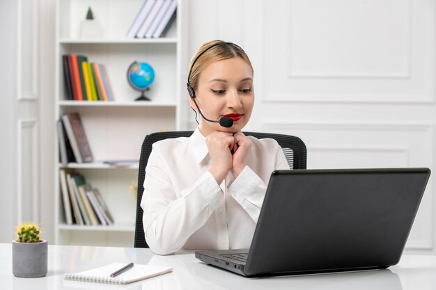 Service à la clientèle jolie fille blonde en chemise blanche avec ordinateur portable et casque mettant les mains sur le menton