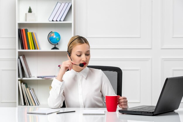 Service à la clientèle jolie fille blonde en chemise blanche avec ordinateur portable et casque parlant sur un microphone