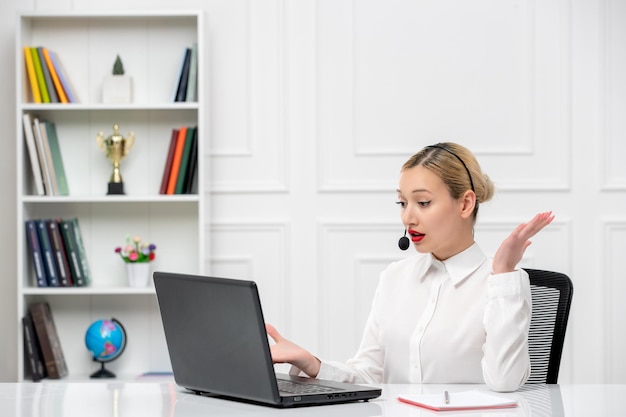 Service à la clientèle jolie fille blonde chemise de bureau avec casque et ordinateur agitant les mains étonnamment