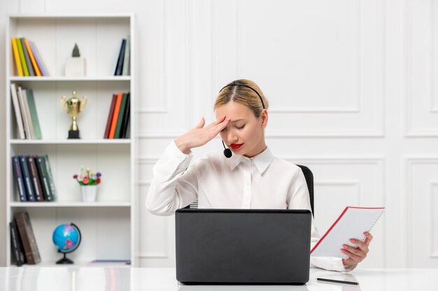 Service à la clientèle jolie fille blonde en chemise de bureau avec casque et ordinateur fatigué