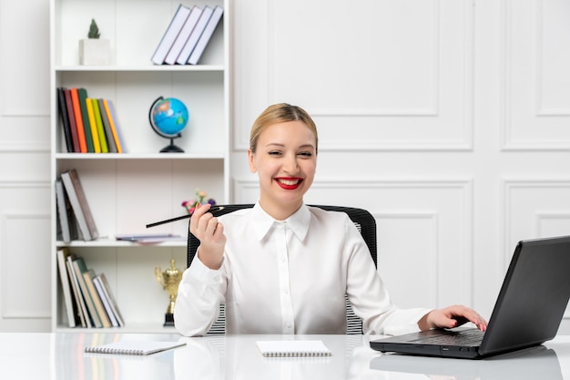 Service à la clientèle jolie fille en chemise blanche avec rouge à lèvres et ordinateur portable souriant et tenant un stylo