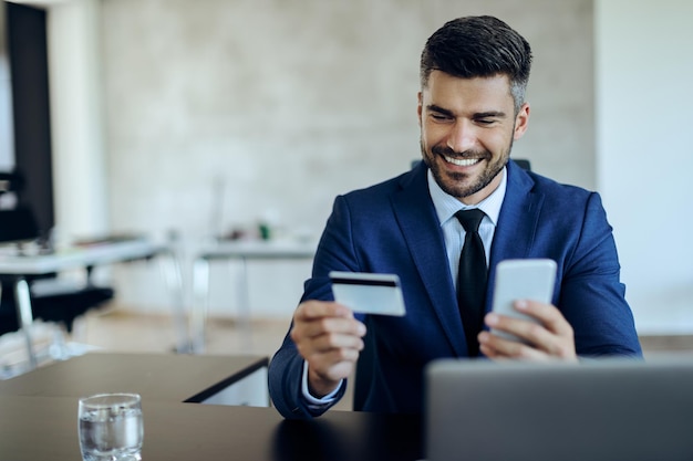 Services bancaires en ligne d'entrepreneur heureux avec carte de crédit et téléphone portable au bureau