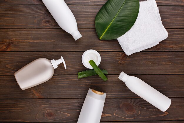 Serviette blanche, bouteilles de shampooing et revitalisant allongé sur une table avec feuille verte et aloès