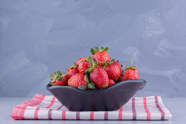 Serviette pliée sous un bol avec un tas de fraises sur fond de marbre. photo de haute qualité