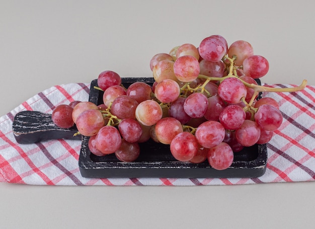 Serviette pliée sous un petit plateau avec des raisins rouges sur marbre