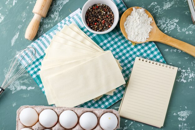 Serviettes avec œufs, grains de poivre, amidon, fouet, rouleau à pâtisserie et cahier