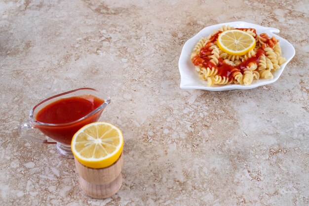 Servir les pâtes avec du citron en tranches et un verre de ketchup sur une surface en marbre
