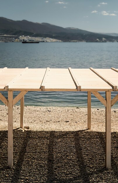 Un seul auvent se dresse sur une plage de galets par une journée ensoleillée Plage de la ville côte de la mer Noire cadre vertical port maritime et montagnes en arrière-plan