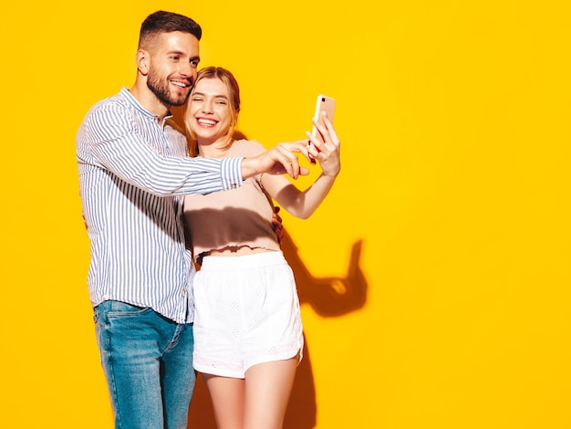 Photo gratuite sexy belle femme souriante et son beau petit ami avoir des moments tendres près du mur jaune en studioregarder l'écran du téléphone portable utiliser des applications pour smartphone choisir des produits dans la boutique en ligne