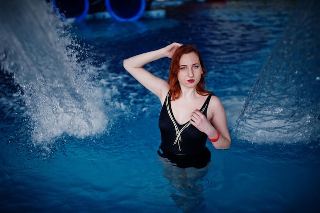 Sexy fille aux cheveux rouges en maillot de bain noir se reposant dans la piscine du parc aquatique