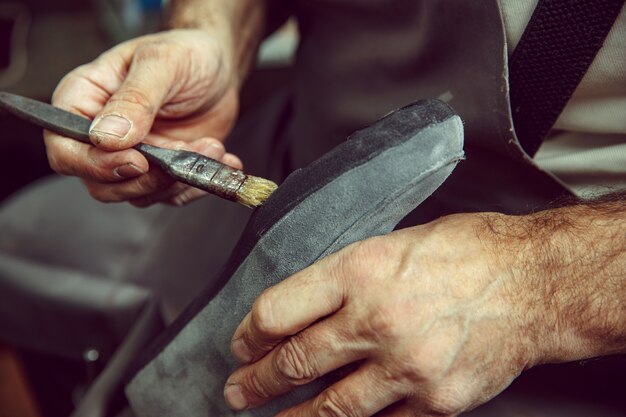 Shoemaker fabrique des chaussures pour hommes. Il enduit un liquide spécial avec un pinceau. L'homme au métier féminin. Concept d'égalité des sexes