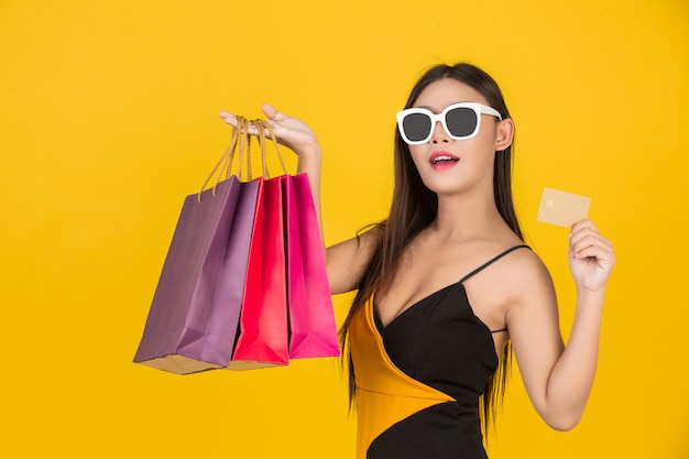 Shopping belle femme portant des lunettes avec une carte de crédit en or avec un sac en papier coloré sur un jaune.