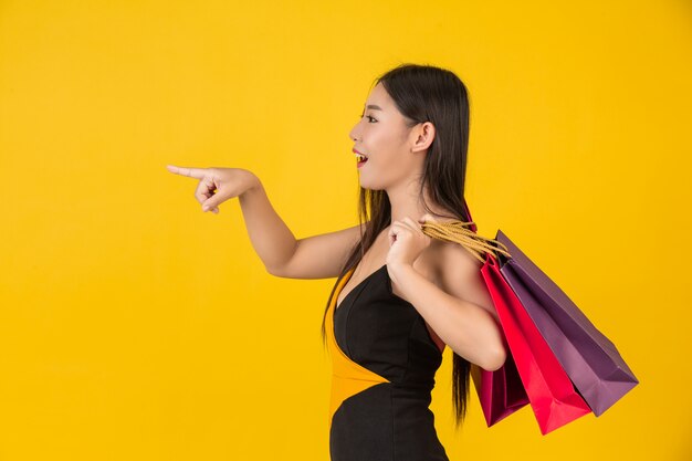 Shopping belle femme tenant un sac en papier coloré sur un jaune.