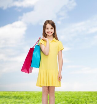 Shopping, bonheur et concept de personnes - petite fille souriante en robe jaune avec des sacs à provisions