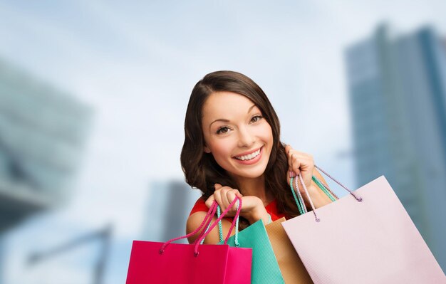 Shopping, vente, cadeaux, noël, concept de noël - femme souriante en robe rouge avec des sacs à provisions