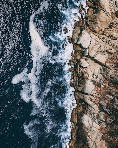 Shot vertical vertical de rivage rocheux à côté d'un plan d'eau avec des vagues éclaboussant les rochers