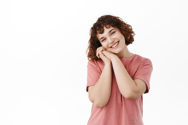 Si jolie. Souriante jolie fille bouclée, s'appuyant sur les paumes et soupirant mignon, regardant quelque chose de beau et de beau, admire quelque chose, rêvassant avec un visage romantique sur blanc