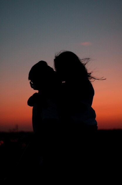 Silhouette du beau couple étreignant contre le coucher de soleil pittoresque coloré