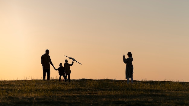 Photo gratuite silhouette familiale complète s'amusant au coucher du soleil