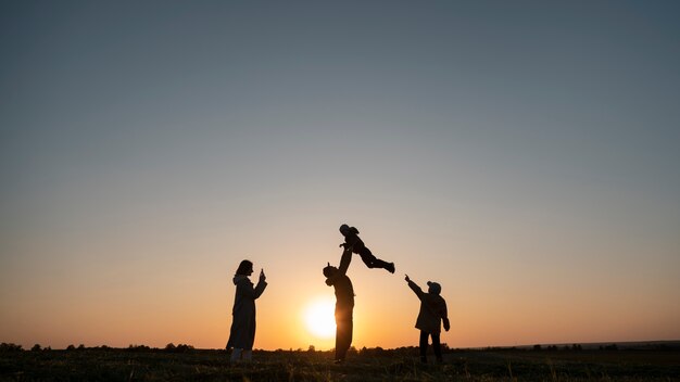 Silhouette familiale complète s'amusant au coucher du soleil