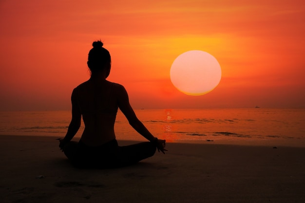 Silhouette de femme faisant du yoga sur une plage