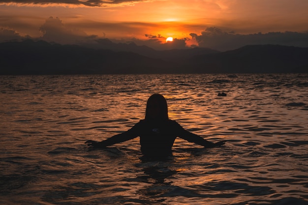 Silhouette d'une femme à moitié dans l'eau d'une mer pendant un beau coucher de soleil