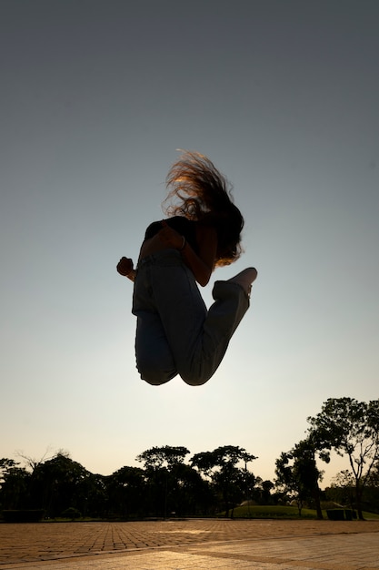 Silhouette de femme plein coup sautant au coucher du soleil