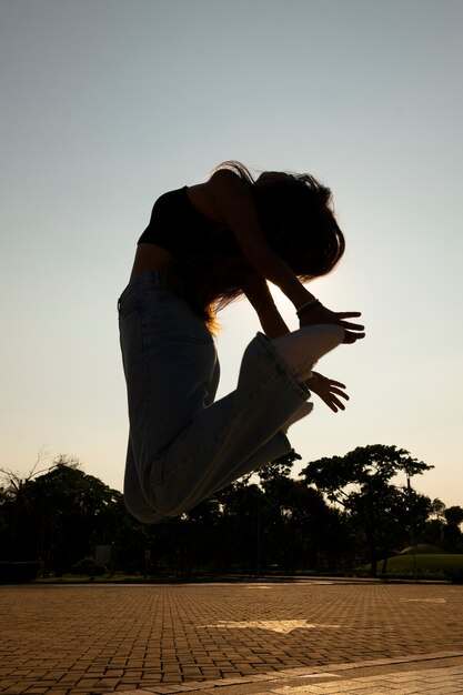 Silhouette de femme plein coup sautant au coucher du soleil